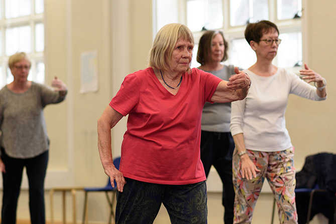 A group of women performing graceful Tai Chi moves in a bright dance studio